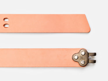 Two tan leather straps are shown. One strap has a pointed end with two holes, while the other end features a metal clasp with three rivets and a prong. Both are set against a white background.