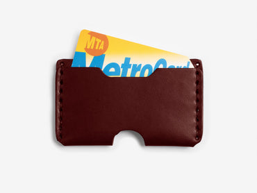 A brown leather card holder with a yellow and blue MTA MetroCard partially visible inside, set against a plain white background.