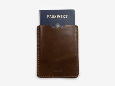 A dark brown leather passport holder with a blue passport partially visible inside, set against a plain white background.