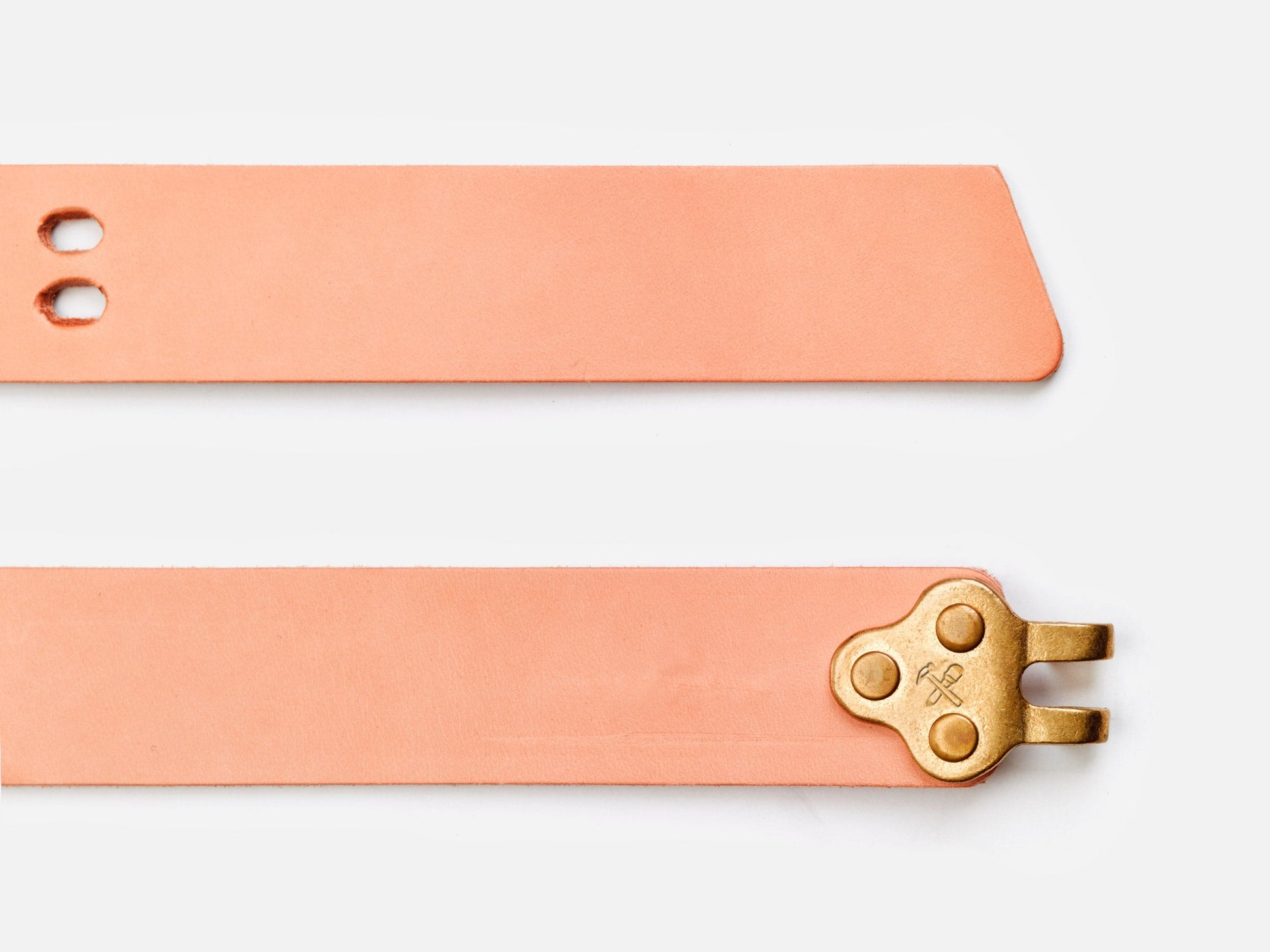 Two strips of light tan leather, one with two holes and a pointed end, the other with a brass buckle attached. Both are set against a plain white background.