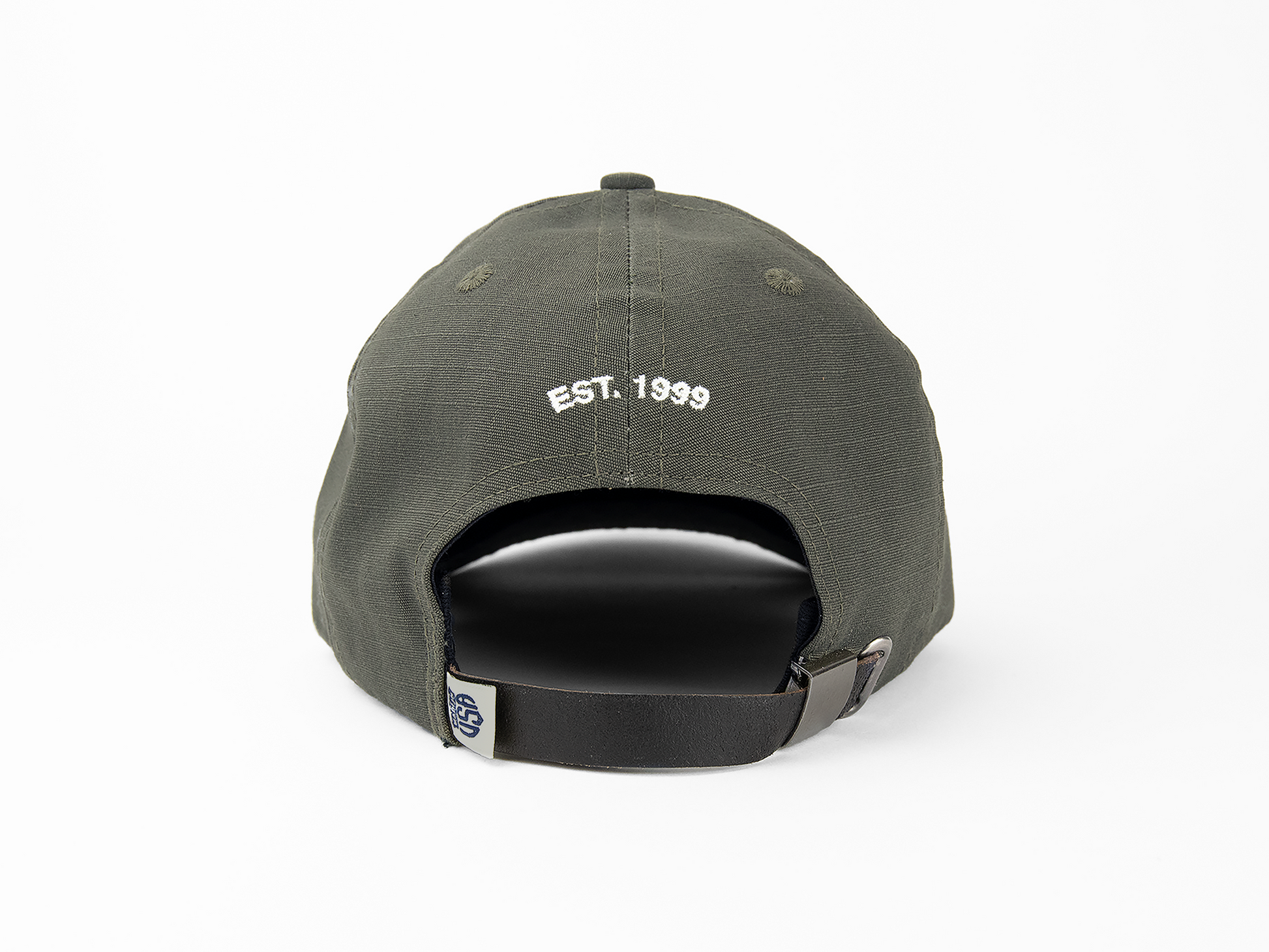 A back view of an olive baseball cap featuring a white embroidery that reads “EST. 1999”. It also features a made in USA woven label and nickel hardware