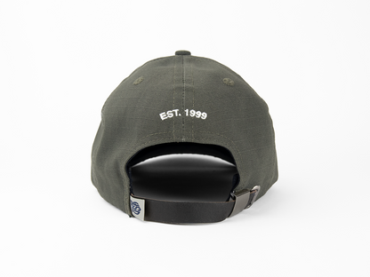 A back view of an olive baseball cap featuring a white embroidery that reads “EST. 1999”. It also features a made in USA woven label and nickel hardware