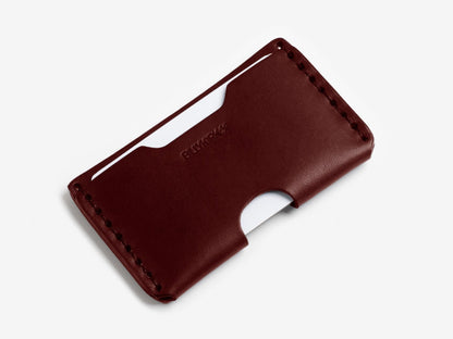 A slim, dark brown leather wallet with visible stitching along the edges, holding two white cards in its slots, displayed on a plain white background.