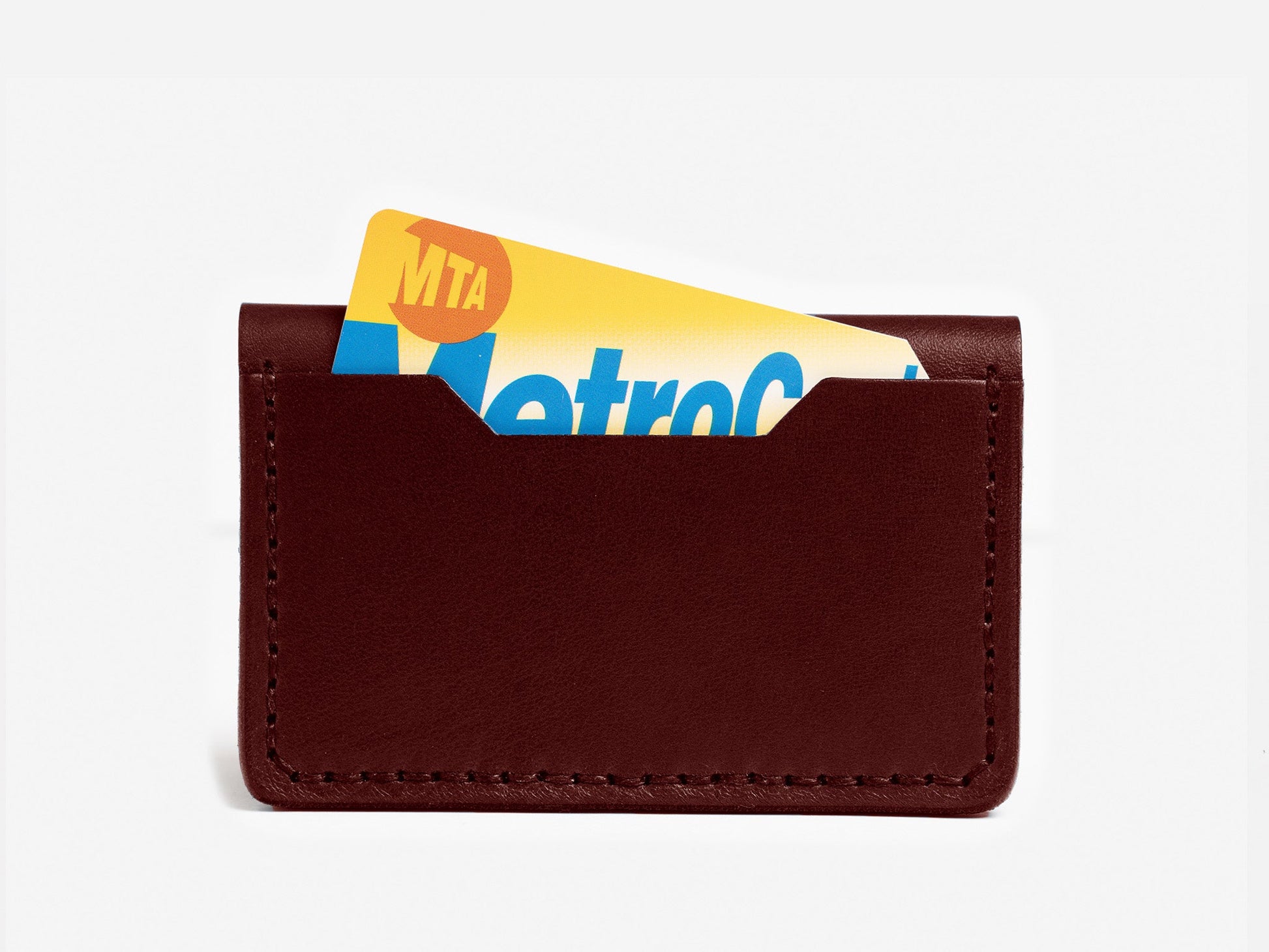 A brown leather card holder with a yellow and blue MTA MetroCard partially visible, inserted into the front pocket, against a plain white background.