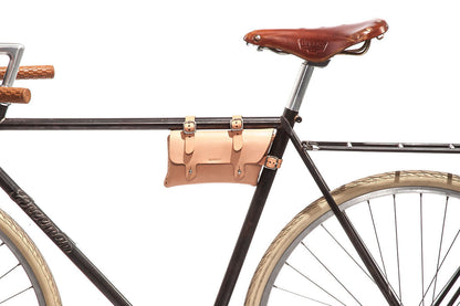 Side view of a black bicycle with tan leather seat, tan leather handlebar grips, white tires, and a small tan leather pouch attached to the frame under the seat against a white background.