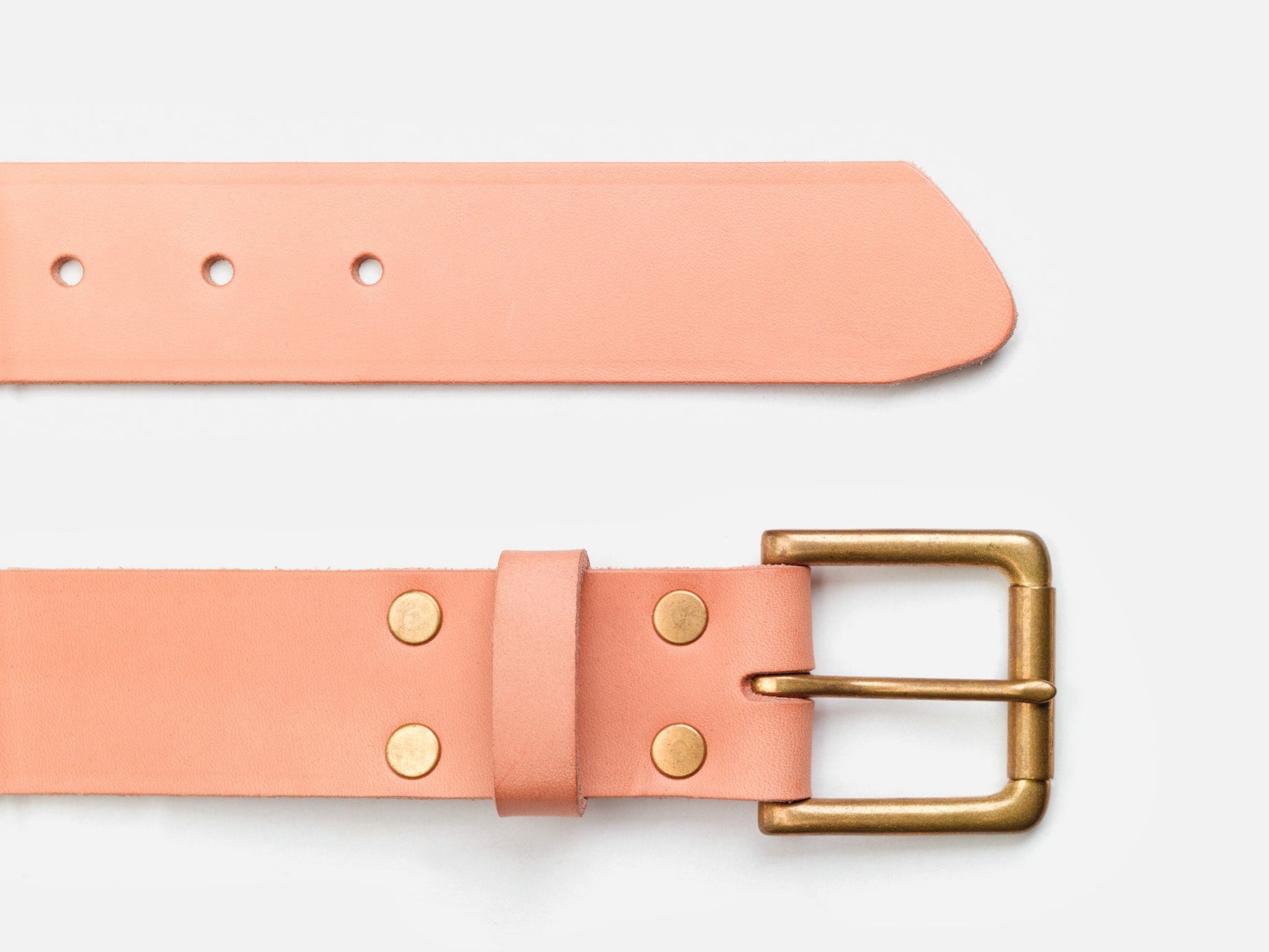 A peach-colored leather belt with a gold rectangular buckle and brass rivets, laid flat on a white background.