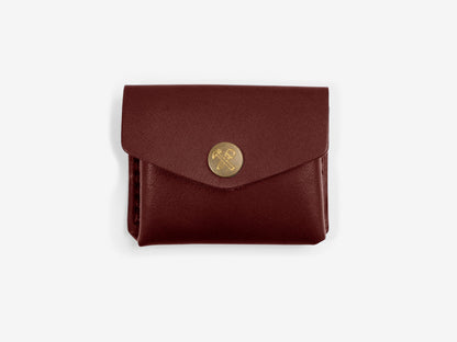 A burgundy leather coin pouch with brass snap closure, displayed with off-white background