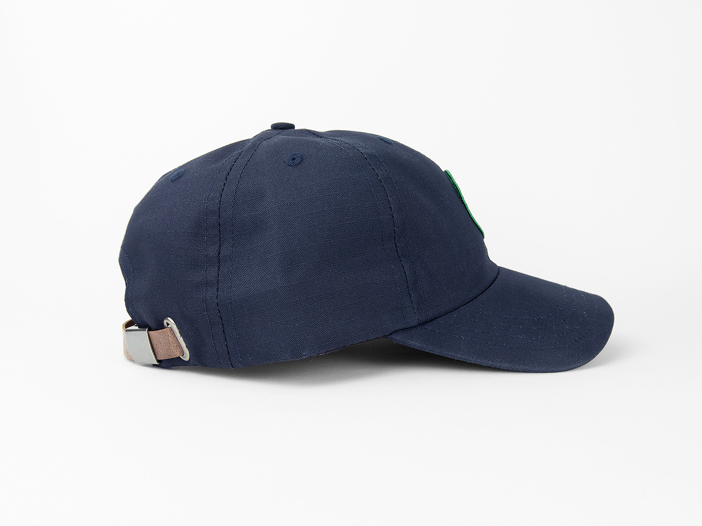 A side view of a navy blue baseball cap showing a leather closing strap and nickel hardware