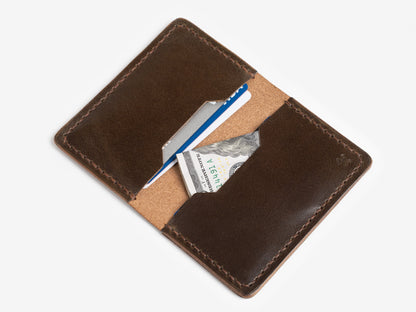 A brown leather wallet open to reveal a blue credit card, a white card, and a folded U.S. twenty-dollar bill against a white background.