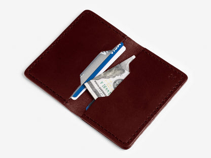 A brown leather wallet open to show a blue credit card, a silver card, and a folded U.S. $100 bill in its card slots, set against a white background.
