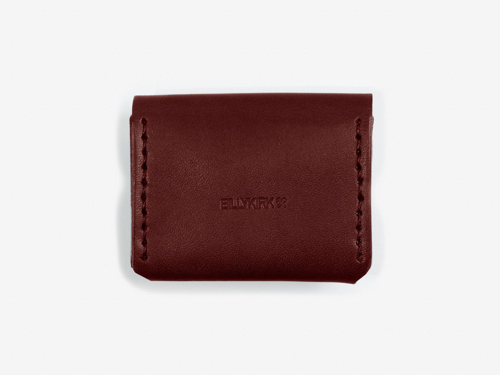 The back of a burgundy leather coin pouch showing the Billykirk logo stamped in the leather on an off-white background