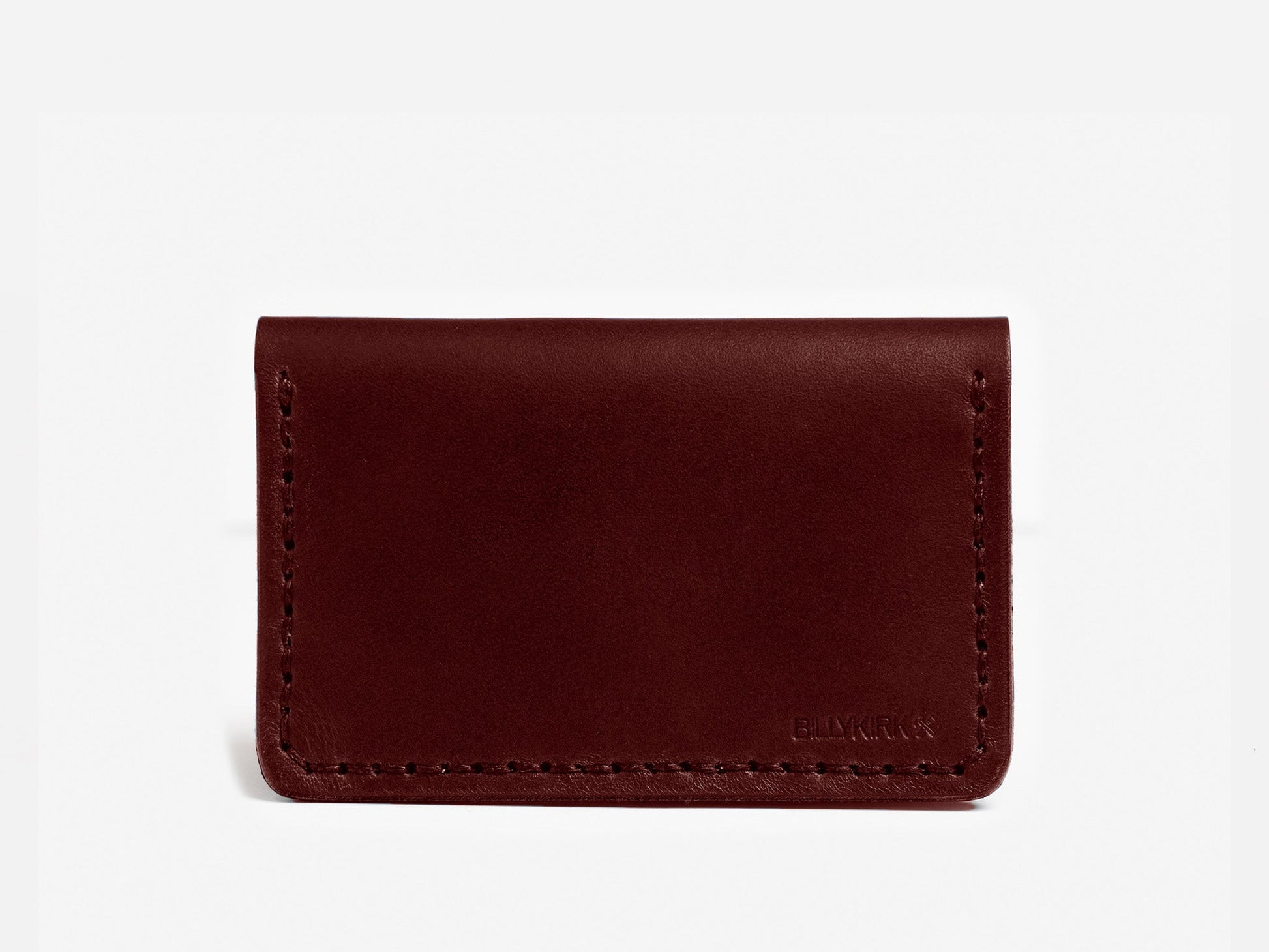 A minimalist, dark brown leather cardholder with visible stitching around the edges, displayed against a plain white background. The lower right corner has a subtle embossed logo.