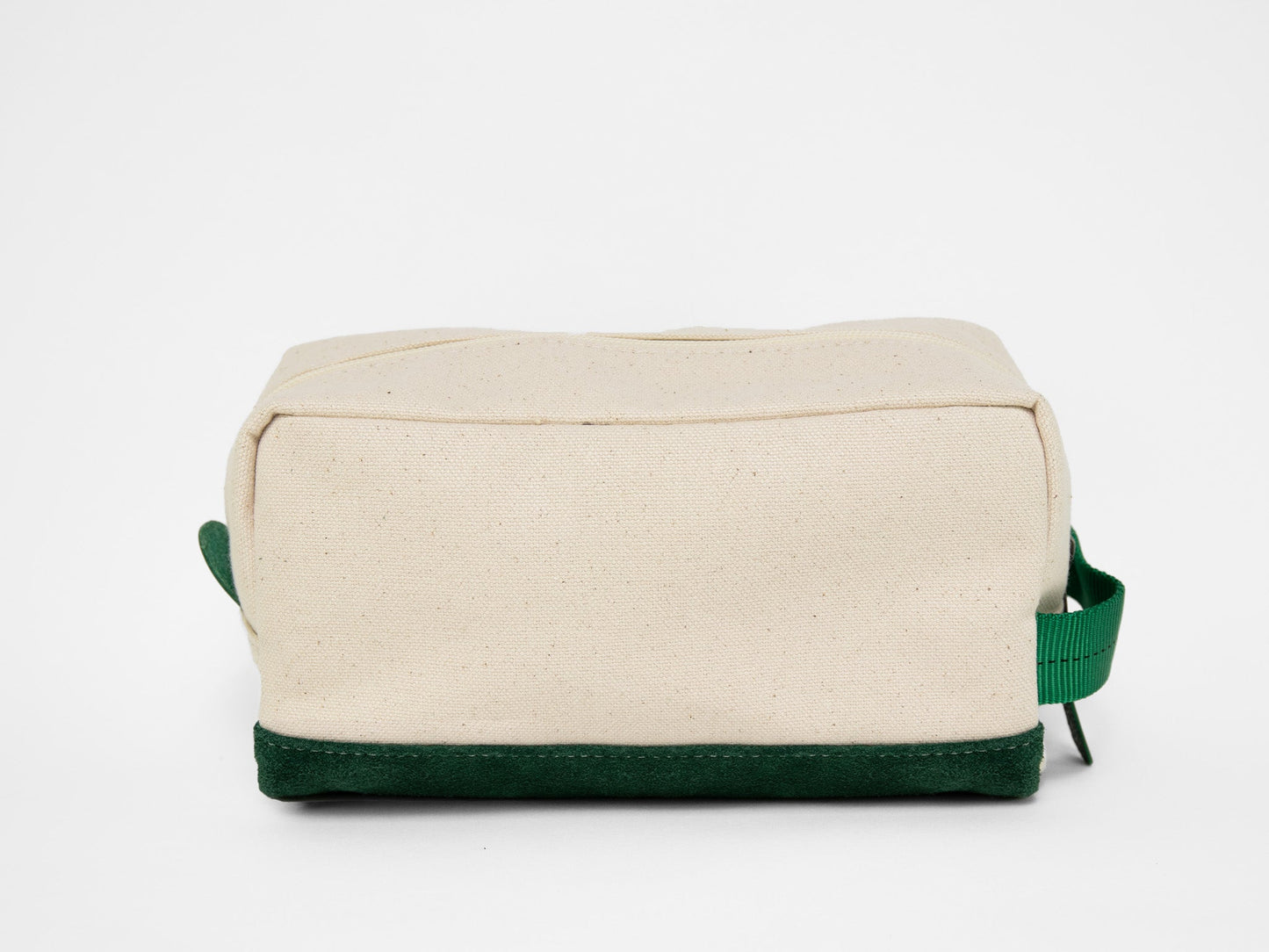 Back view of a rectangular natural canvas toiletry bag with zipper closure, green webbing handle, and suede green base.