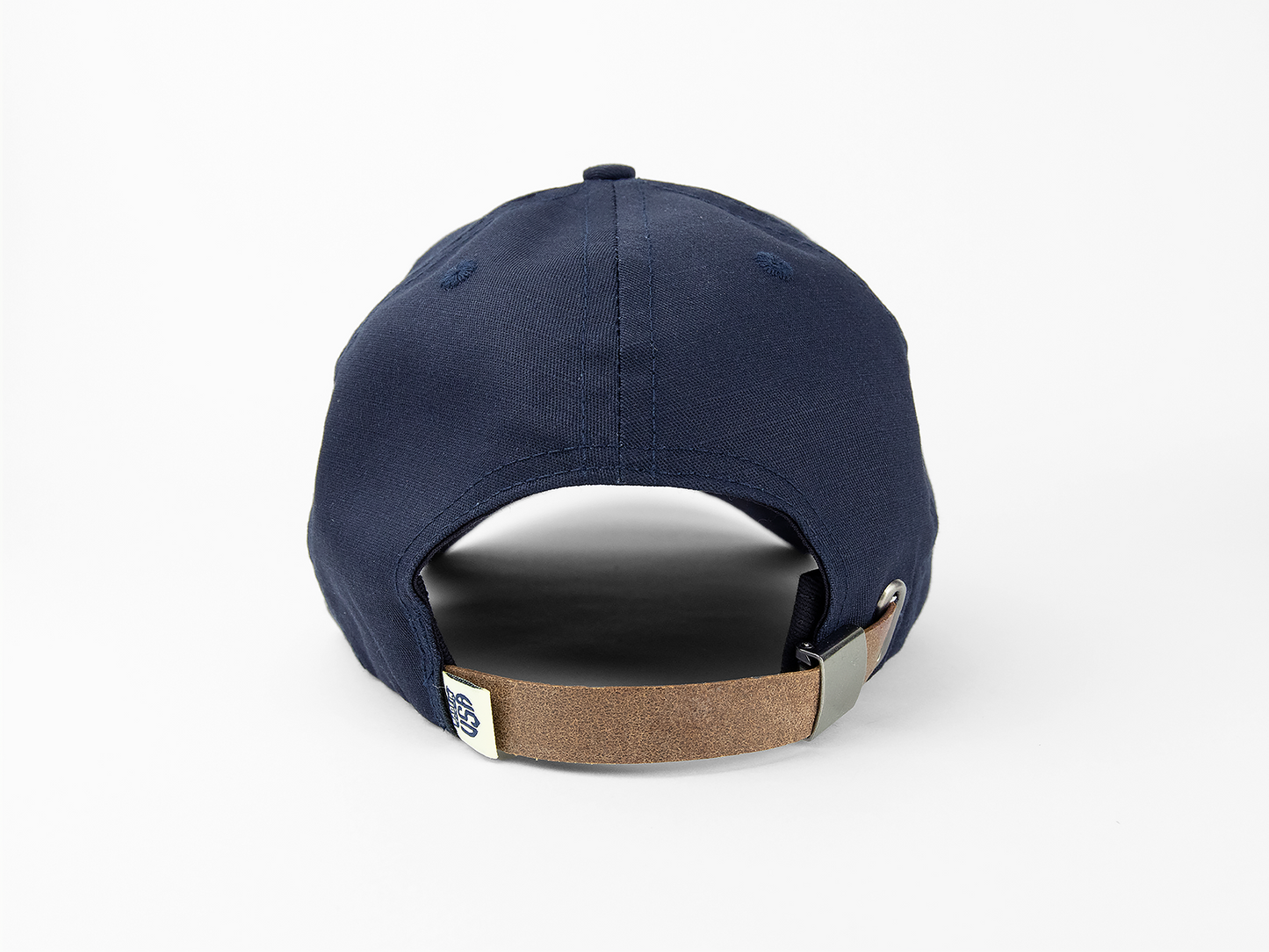 A back view of a navy blue baseball cap showing a leather closing strap, made in usa woven tag, and nickel hardware
