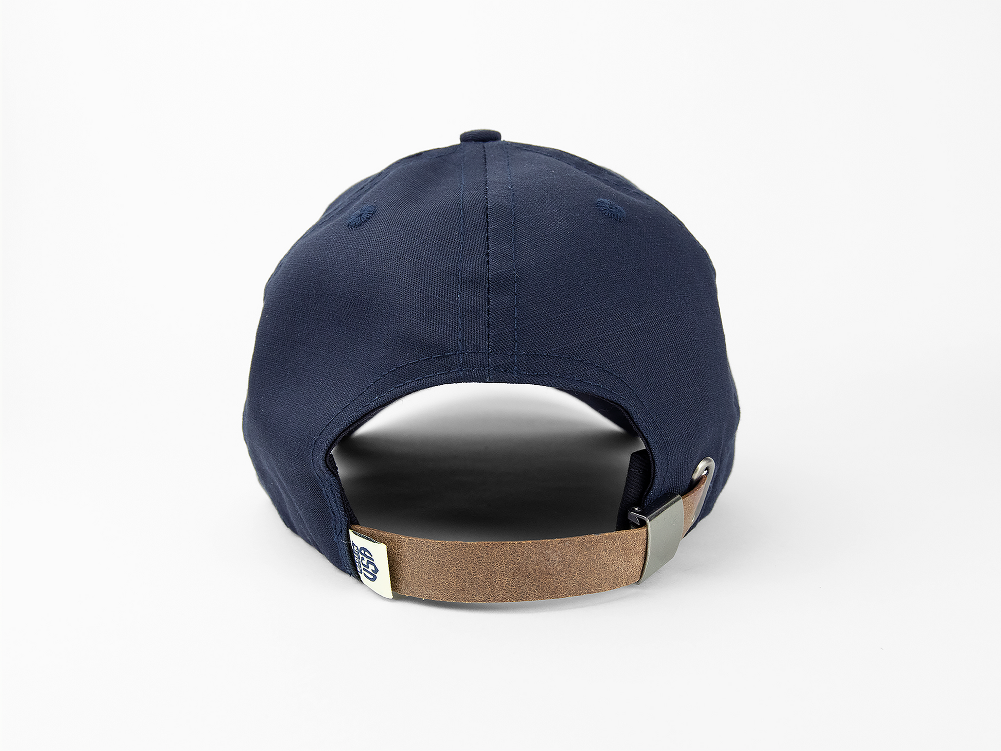 A back view of a navy blue baseball cap showing a leather closing strap, made in usa woven tag, and nickel hardware