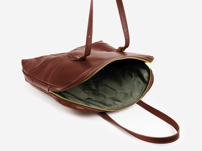 A brown leather tote bag with two handles and a yellow zipper, shown open to reveal a spacious green fabric-lined interior on a white background.