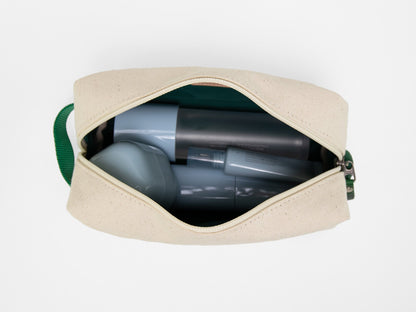 A beige zippered pouch with a green handle, partially open to show several gray and silver cylindrical and hexagonal bottles inside, viewed from above on a white background.