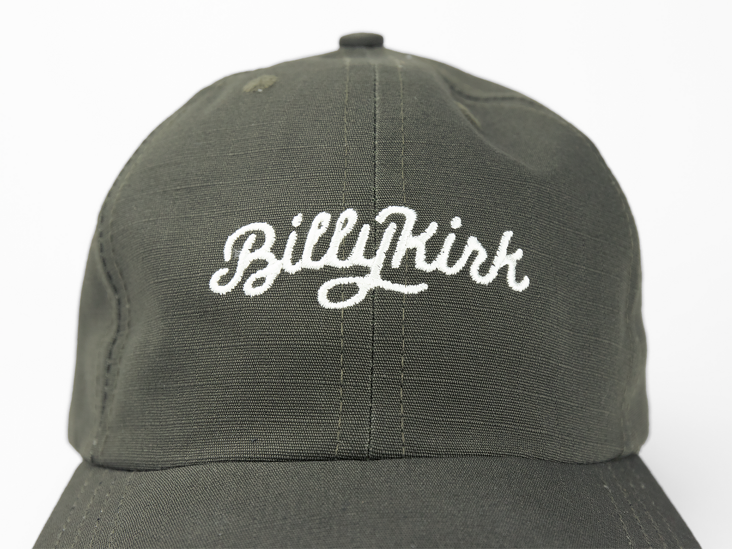 An olive baseball cap featuring a white cursive embroidery on the front that reads “Billykirk”.