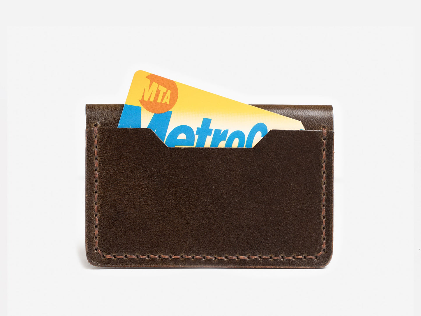 A brown leather card holder with a New York City MTA MetroCard partially inserted and visible against a white background.