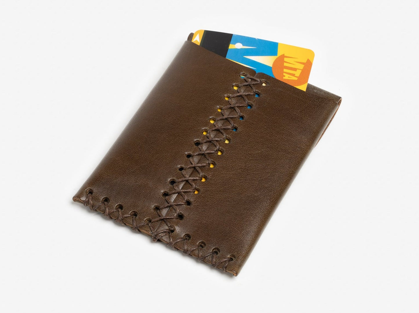 A brown leather wallet with decorative stitching, holding two cards, one of which is a yellow and orange MTA transit card. The wallet is placed on a white background.