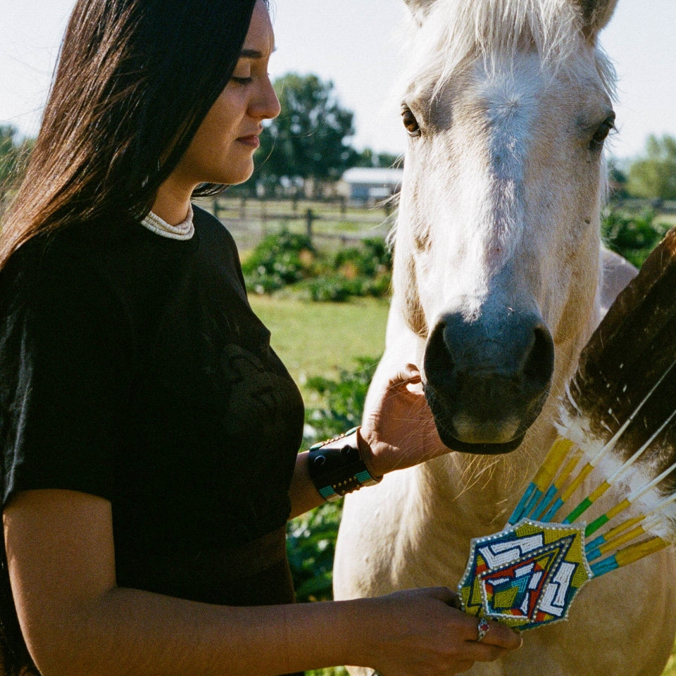 Indigenous Ginew's black cotton  thunderbird t-shirt on Native American women with white horse