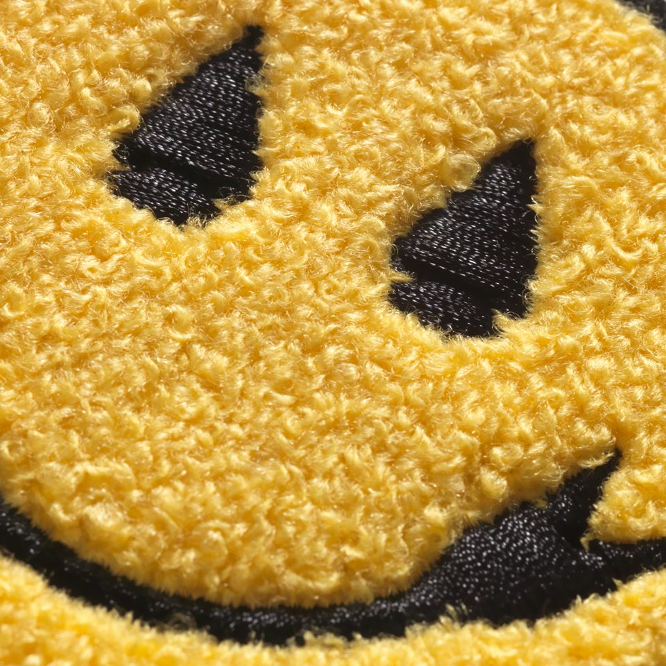 Close up of Chenille smiley face sew on patch designed by Native American Steven Paul Judd with arrowhead smile and eyes. 