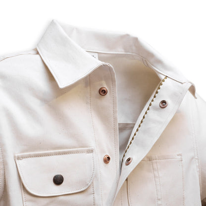 A natural seed chore coat with snap buttons, featuring a collar, front pockets, and shelling detail