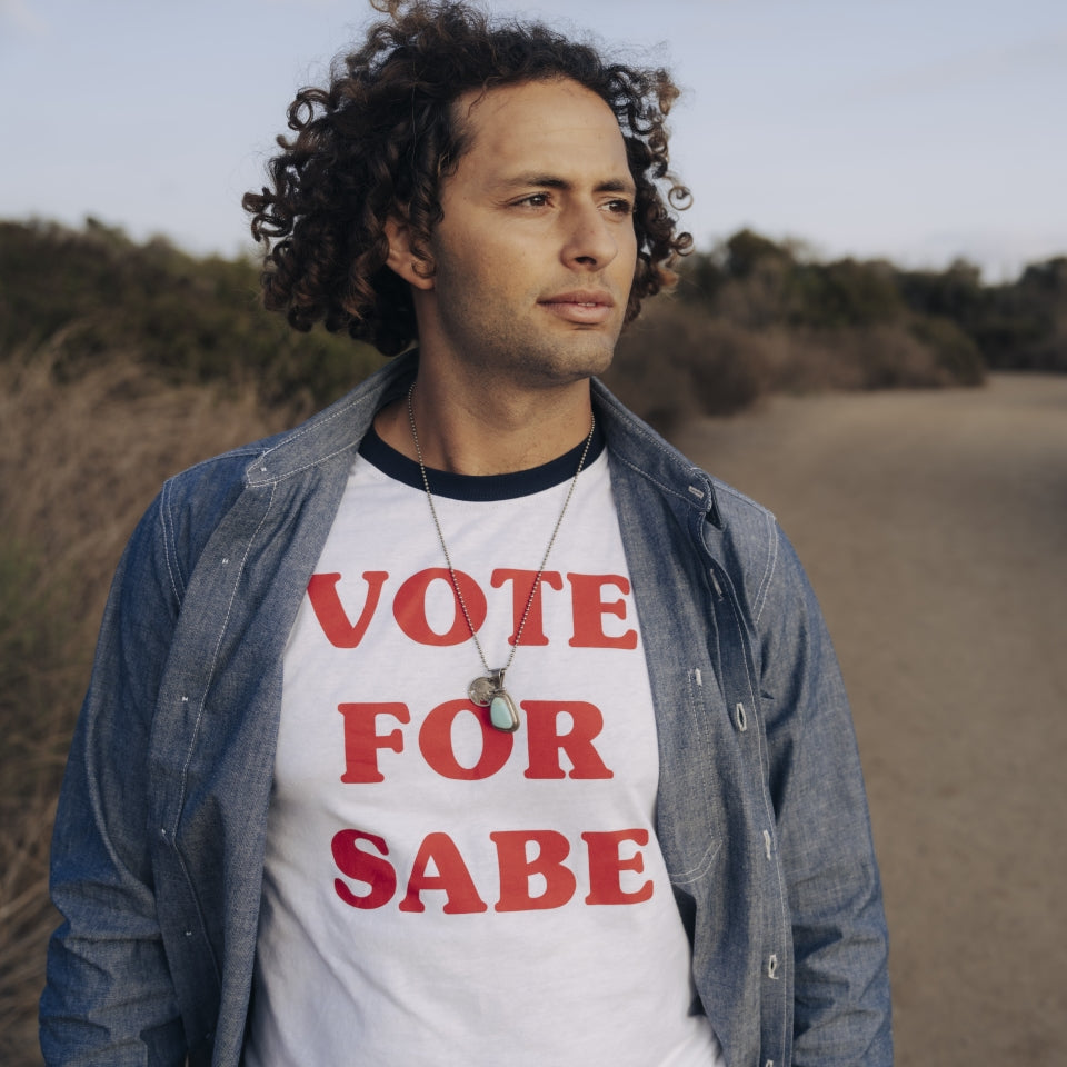 Man wearing a Vote for bigfoot Sabe t-shirt layered with chambray button down shirt in blue